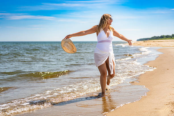 Beautiful middle-aged woman in swimsuit walking against background of blue sky in summertime.